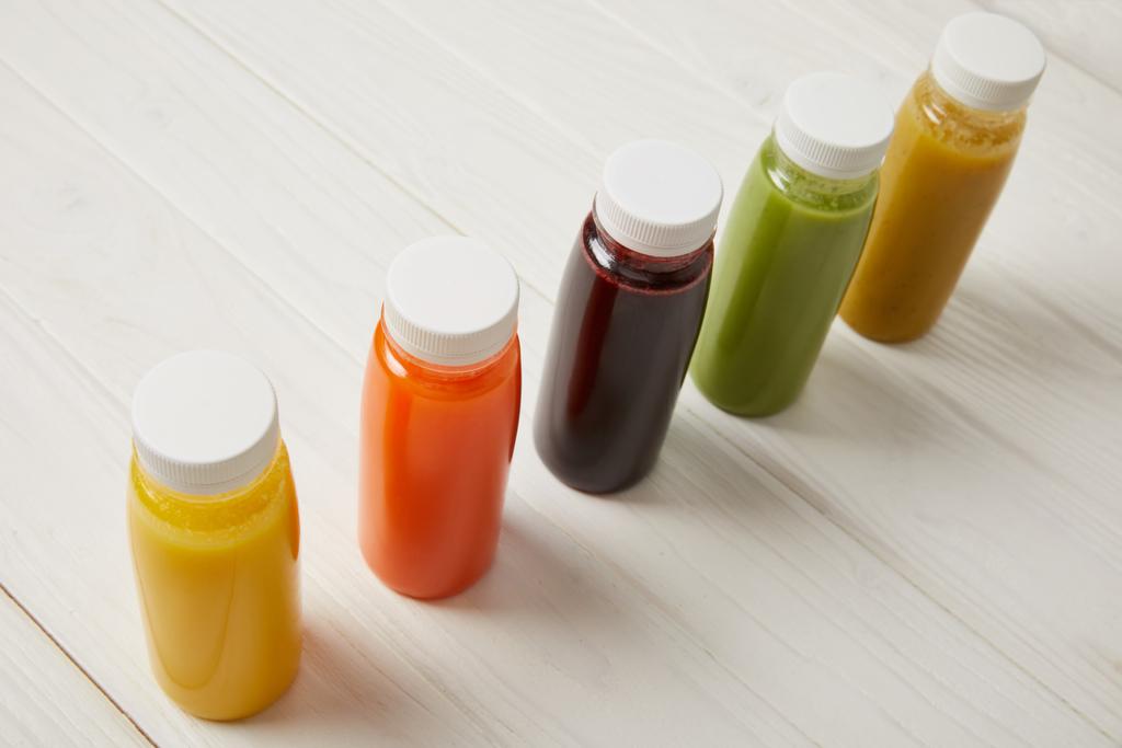 Детоксичні смузі в пляшках, що стоять в ряд на білому дерев'яному фоні
   - Фото, зображення