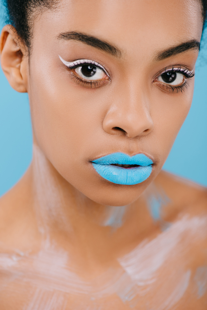 lähikuva muotokuva nuori afrikkalainen amerikkalainen nainen luova meikki ja täydellinen iho katselee kameran eristetty sininen
 - Valokuva, kuva