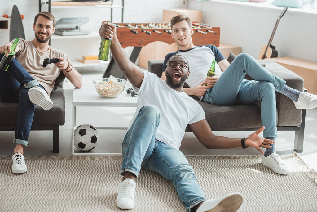 üç çok kültürlü gençler salon futbol maçı izlerken ve bira şişeleri ile kutluyor  - Fotoğraf, Görsel