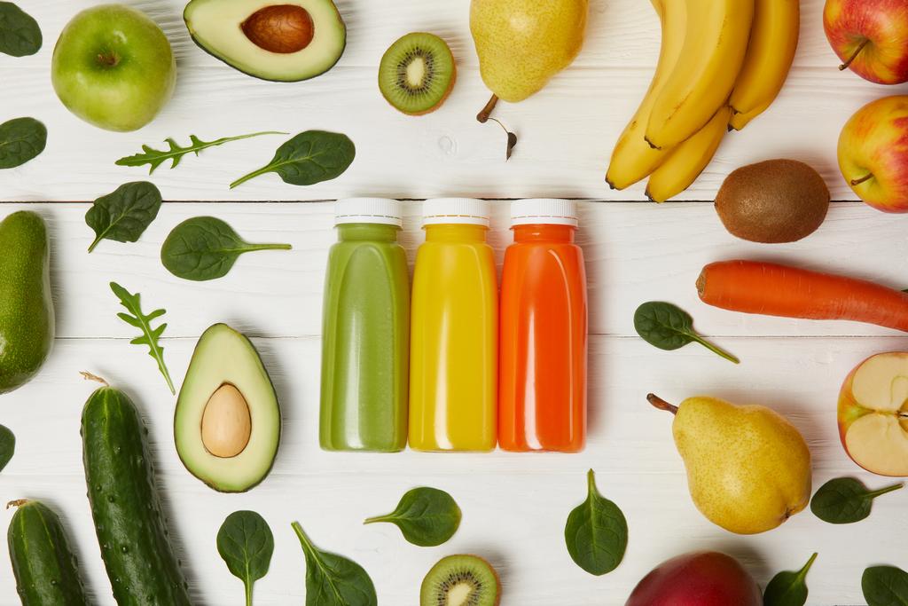 vlakke leggen met flessen met detox smoothies in rij met fruit en groenten op houten achtergrond - Foto, afbeelding