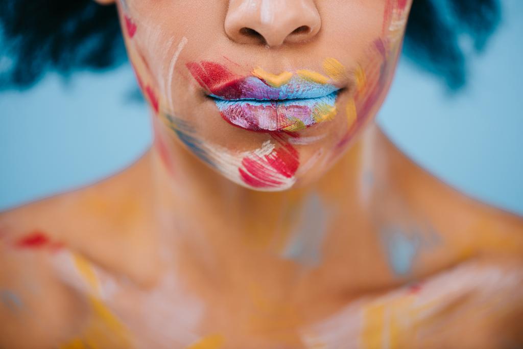 bijgesneden schot van vrouw met penseelstreken op gezicht op blauw - Foto, afbeelding