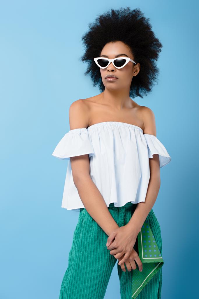 jovem afro-americana em elegante off-the-ombro top e óculos de sol isolados em azul
 - Foto, Imagem