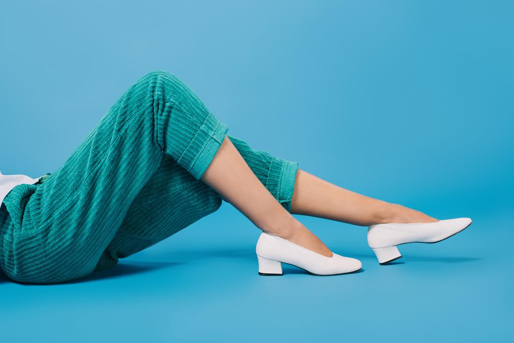 スタイリッシュなパンツと靴が青い床に横になっている女性のクロップ撮影 - 写真・画像