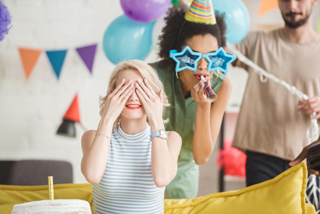 Молодой человек и женщина приветствуют блондинку с праздничным тортом на вечеринке-сюрпризе
 - Фото, изображение