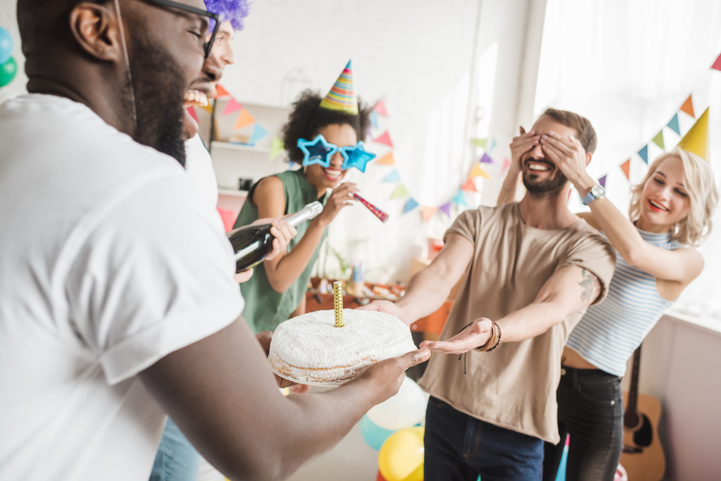 Festeggiare persone diverse che coprono gli occhi del giovane amico e lo salutano con la torta di compleanno
 - Foto, immagini