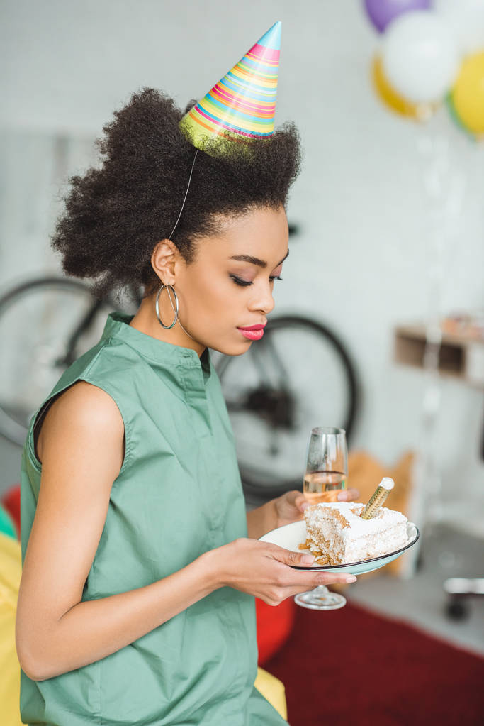 afro-americano donna in partito cappello in possesso di piatto con torta a casa festa
 - Foto, immagini