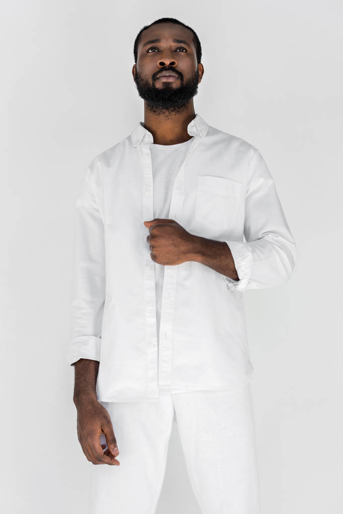 χαμηλή γωνία θέα όμορφος μοντέρνος αφρικανική αμερικανική άνθρωπος unbuttoning λευκό πουκάμισο απομονωθεί σε λευκό - Φωτογραφία, εικόνα