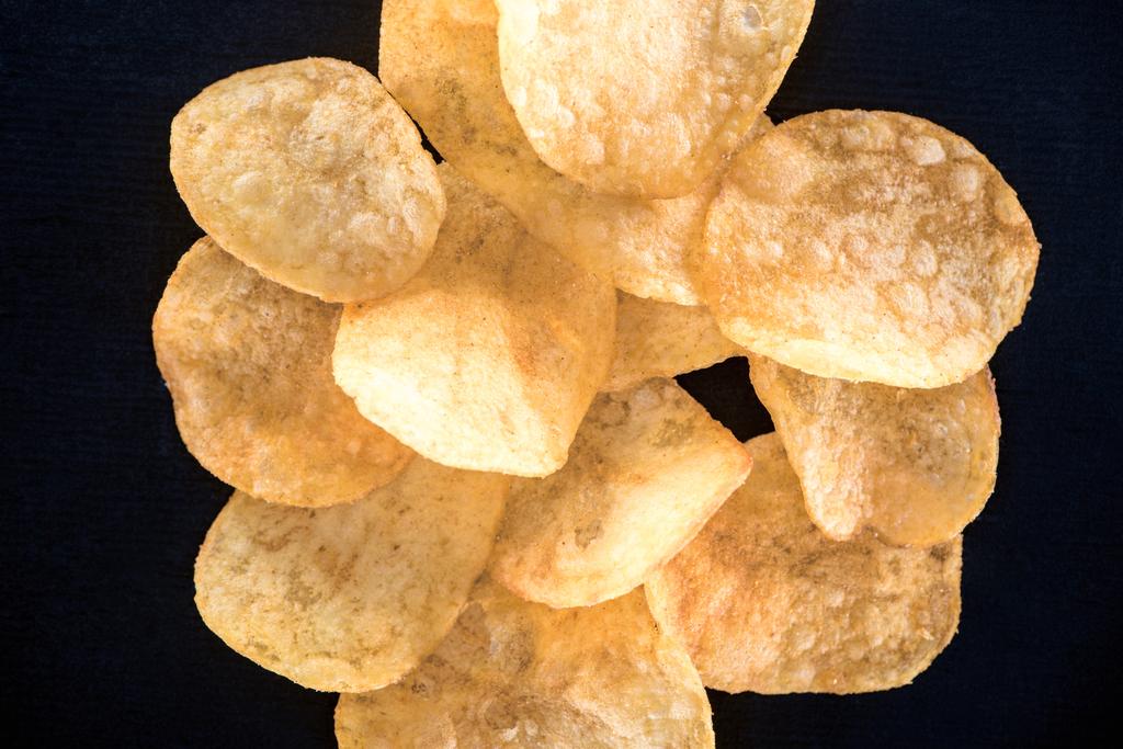 zbliżenie, chrupiące niezdrowych chipsów ziemniaczanych na czarnym tle - Zdjęcie, obraz