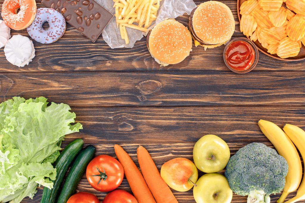 вид на свежие фрукты с овощами и разнообразные нездоровые продукты на деревянном столе
  - Фото, изображение