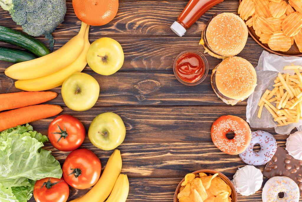 pohled shora čerstvé zralé ovoce, zeleninu a různé nezdravé potraviny na dřevěný stůl  - Fotografie, Obrázek