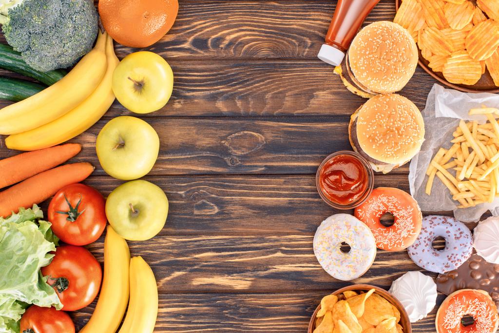 pohled shora čerstvé zralé ovoce, zeleninu a různé nezdravé potraviny na dřevěný stůl - Fotografie, Obrázek