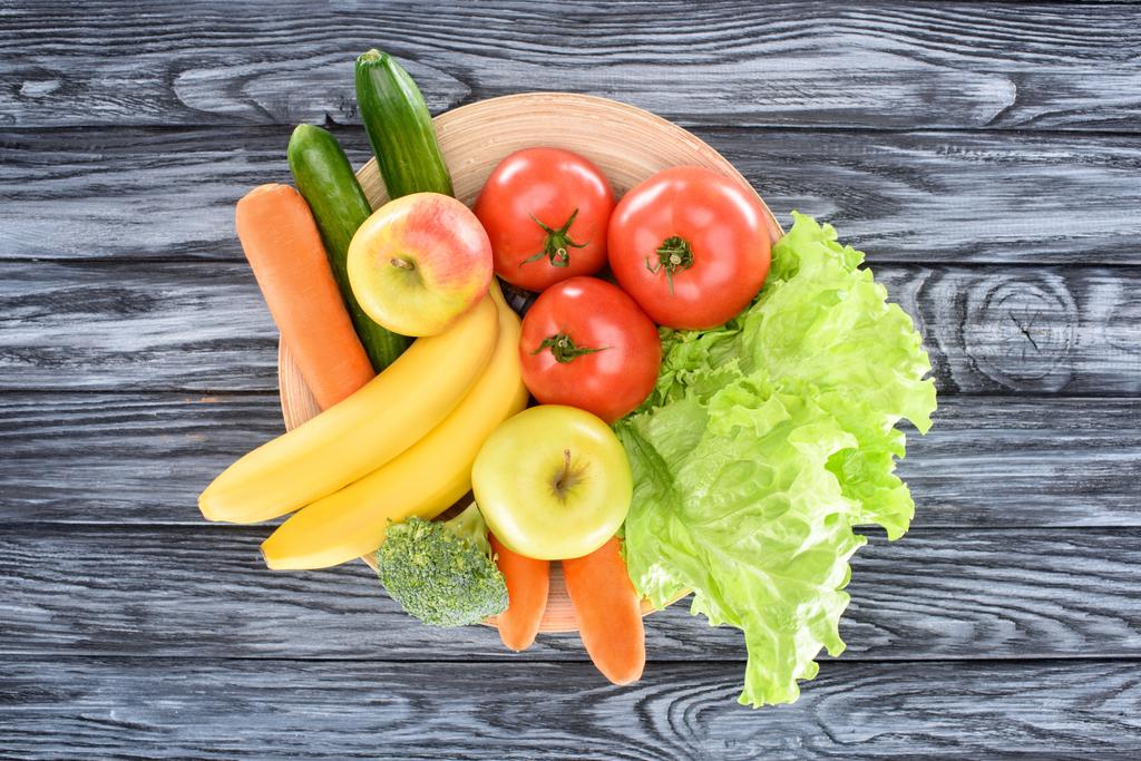 Blick von oben auf frisches reifes Obst und Gemüse auf Teller auf Holztisch - Foto, Bild