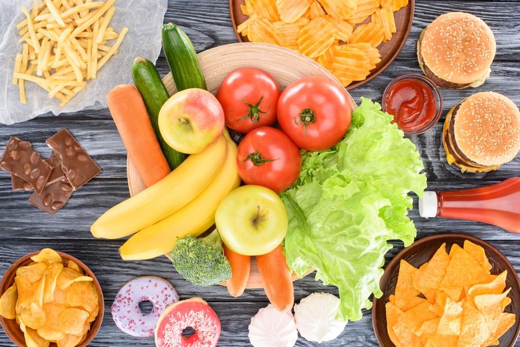 вид зверху асортиментованої нездорової їжі та свіжих фруктів з овочами на дерев'яному столі
    - Фото, зображення