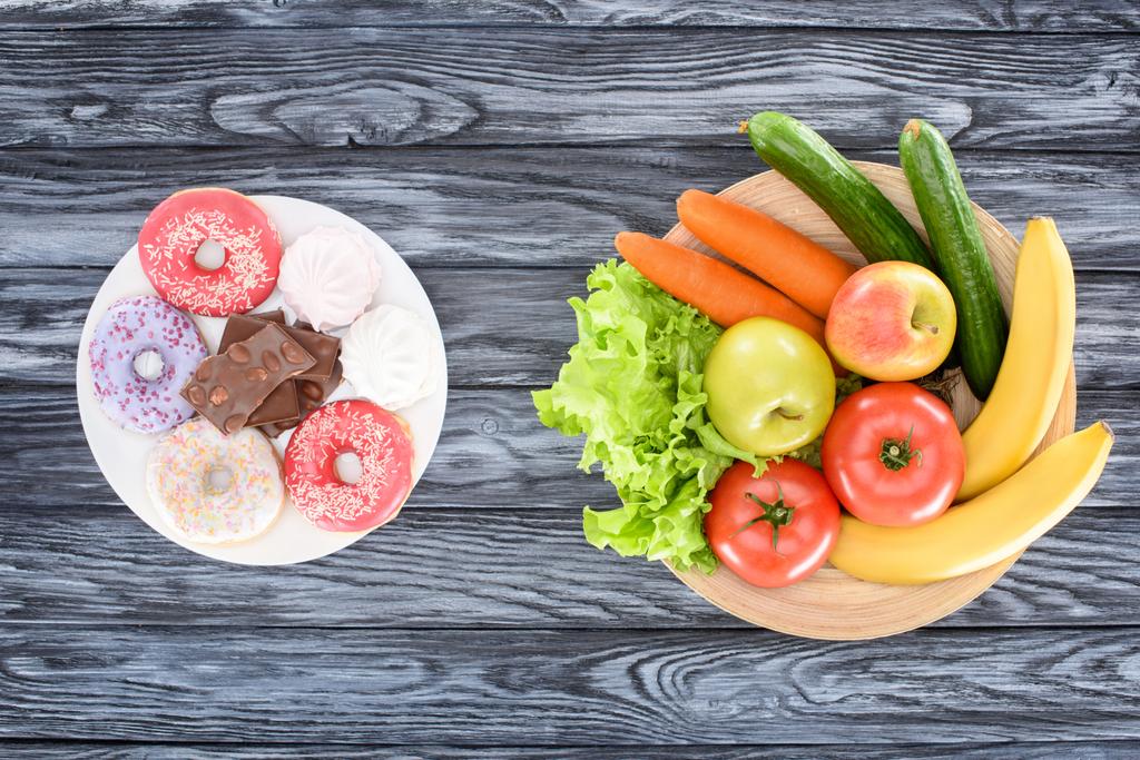 Blick von oben auf frisches Obst mit Gemüse und Süßigkeiten auf Holztisch - Foto, Bild