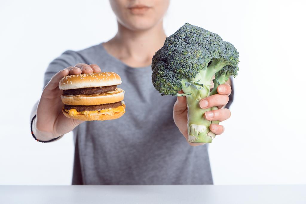 vue rapprochée de la femme tenant un brocoli frais mûr et un hamburger
  - Photo, image