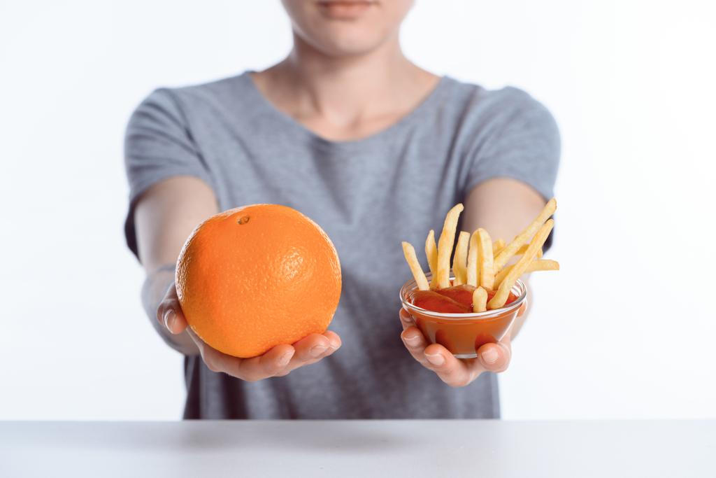 обрізаний знімок дівчини, що тримає стиглий апельсин і кетчуп з картоплею фрі
  - Фото, зображення