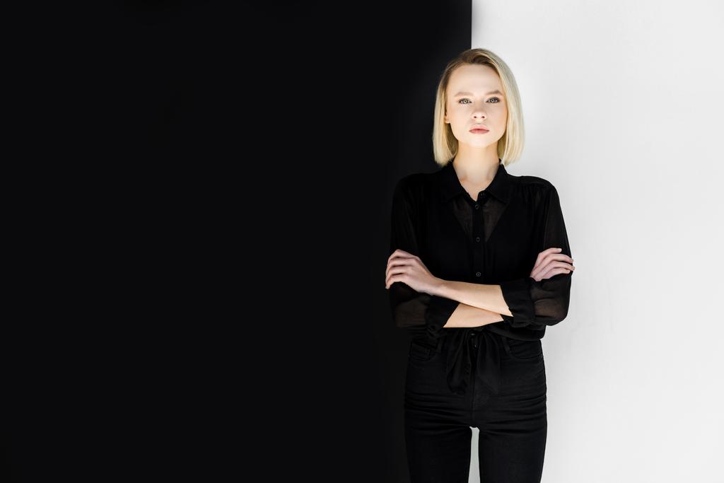 houkutteleva tyylikäs blondi nainen mustissa vaatteissa seisoo ristissä kädet
 - Valokuva, kuva