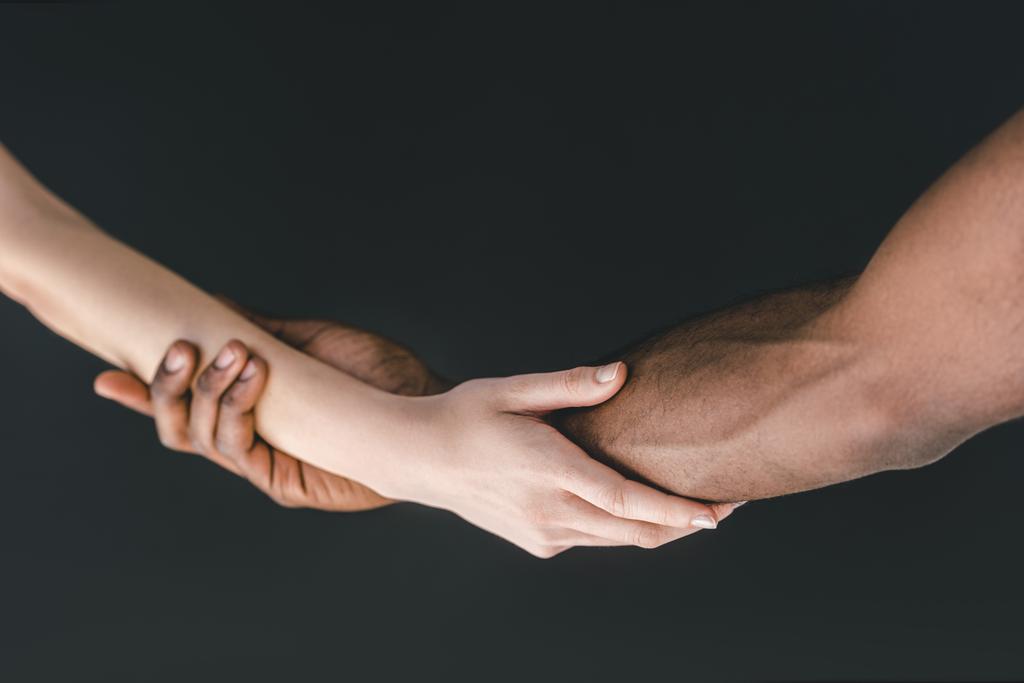 περικομμένη εικόνα της πολυπολιτισμικής ζευγάρι κρατώντας τα χέρια που απομονώνονται σε μαύρο - Φωτογραφία, εικόνα