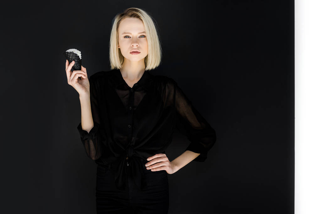attraktive, stylische blonde Frau in schwarzer Kleidung mit Eis in schwarzem Kegel - Foto, Bild