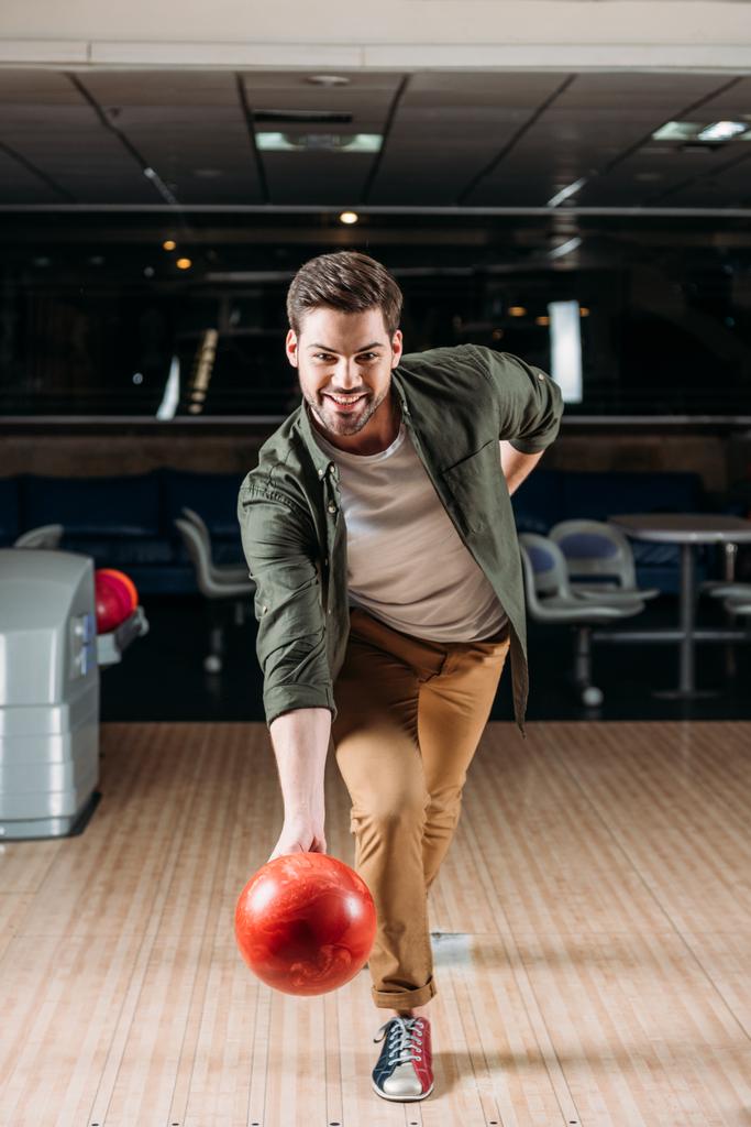 šťastný mladý muž vrhací bowlingové koule v klubu - Fotografie, Obrázek
