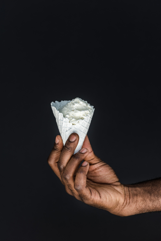 περικομμένη εικόνα αφρικανική αμερικανική άνθρωπος που κρατά το άσπρο παγωτό χωνάκι που απομονώνονται σε μαύρο - Φωτογραφία, εικόνα