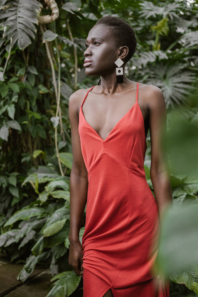 beautiful stylish african american girl with short hair posing in red dress in garden - Photo, Image
