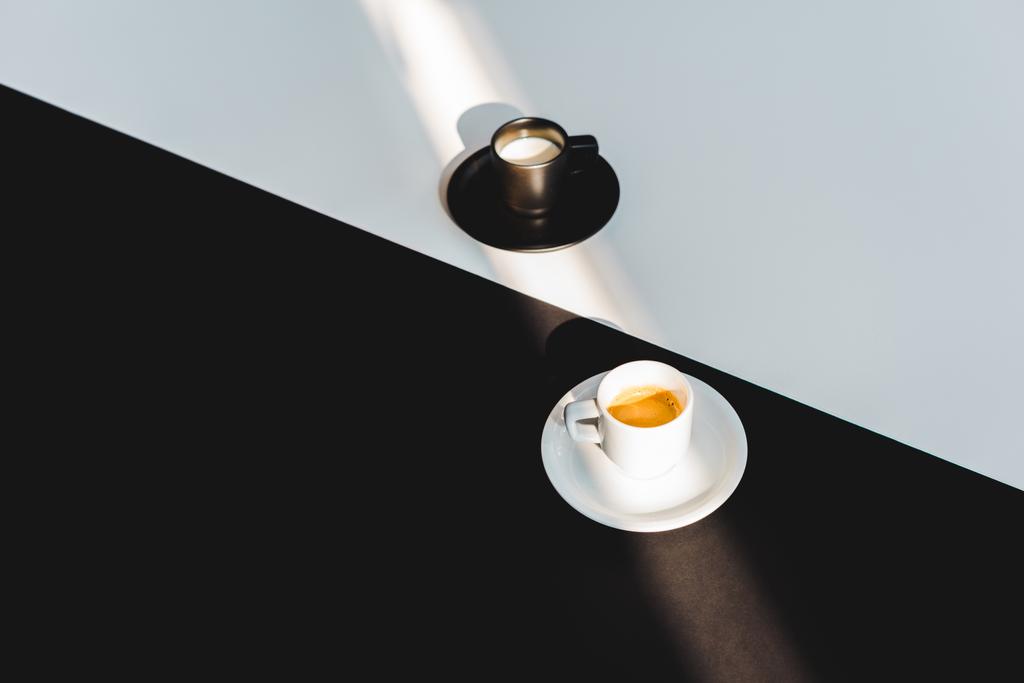 Hochwinkelaufnahme von schwarzen und weißen Tassen Milch und Kaffee auf schwarzer und weißer Oberfläche, Yin-Yang-Konzept - Foto, Bild