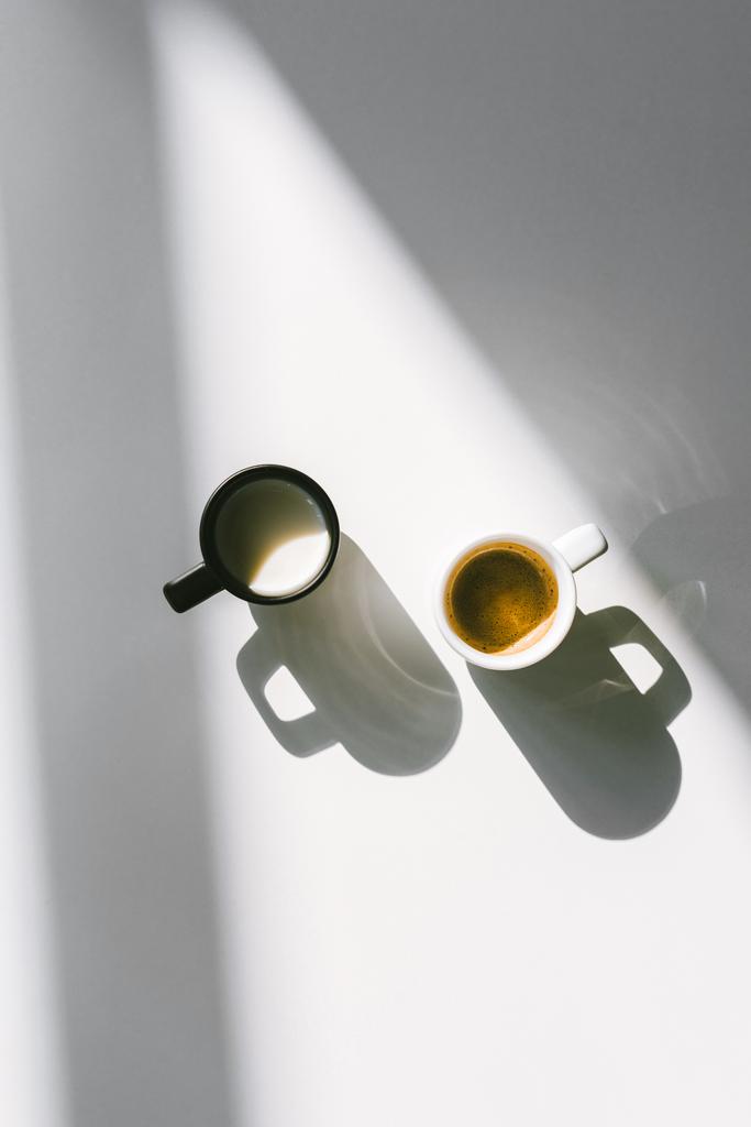 vista superior de copos pretos e brancos de leite e café na superfície branca
 - Foto, Imagem