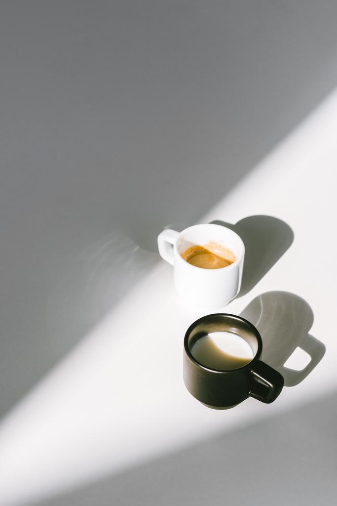 vista de alto ângulo de copos pretos e brancos de leite e café na superfície branca
 - Foto, Imagem