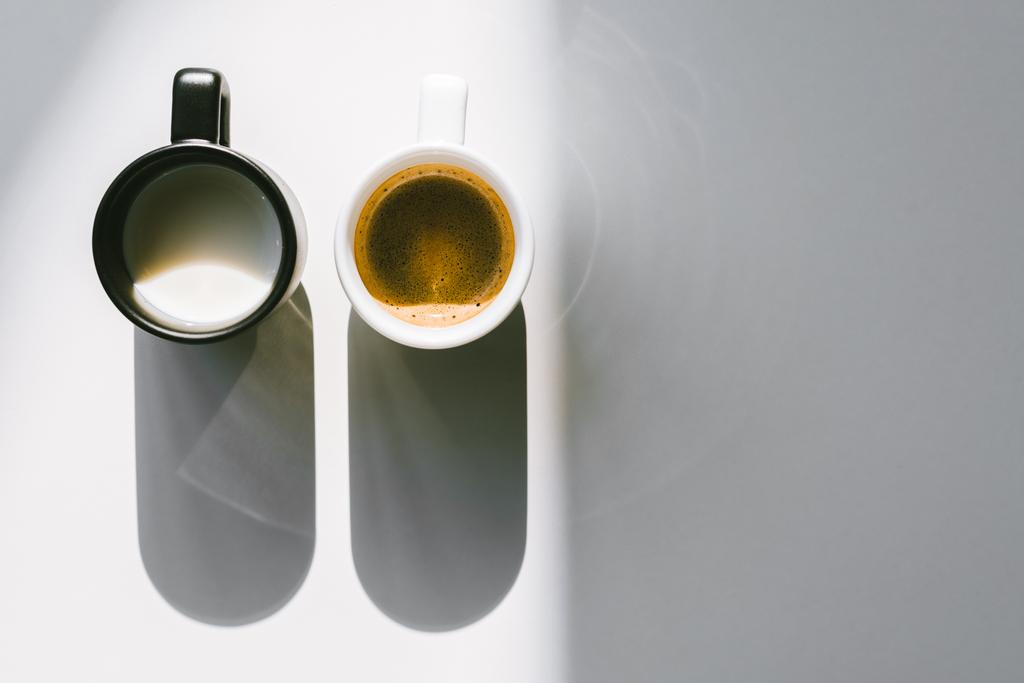 Ansicht von Schwarz-Weiß-Tassen mit Milch und Kaffee auf weißer Tischplatte - Foto, Bild