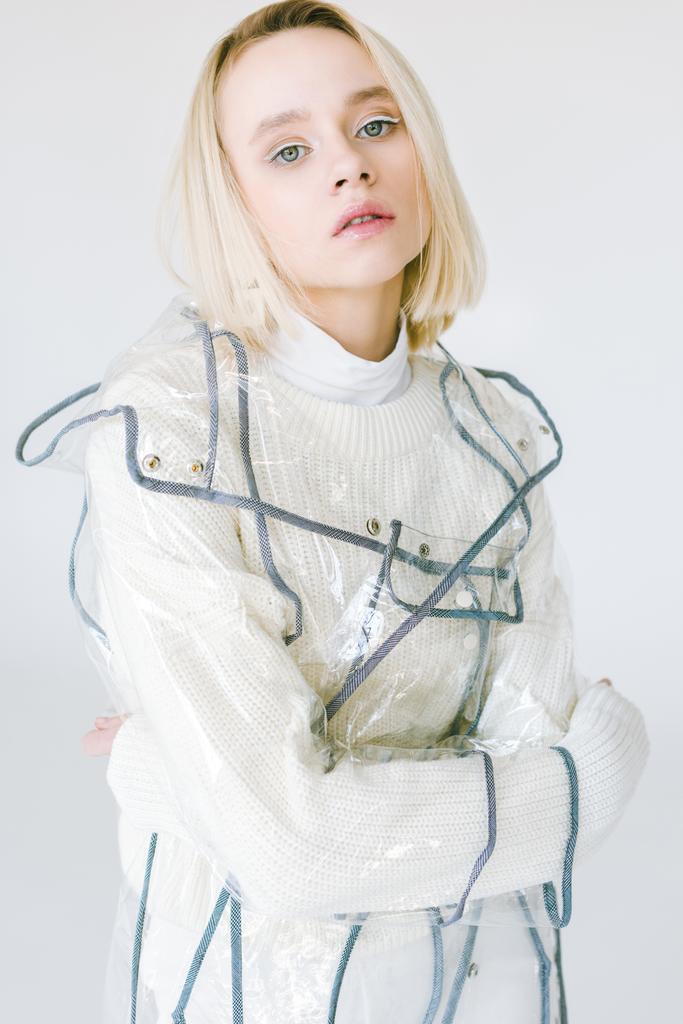 красивая стильная блондинка в белой одежде и прозрачном пальто, смотрящая на камеру, изолированную на белом
 - Фото, изображение