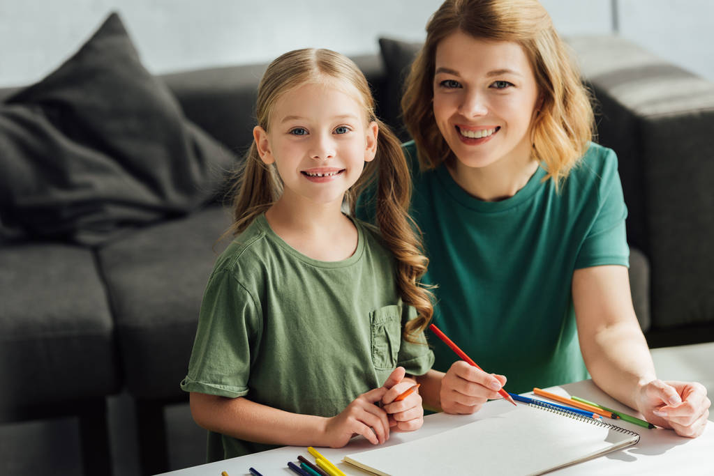 heureux mère et fille dessin avec crayons de couleur et sourire à la caméra
 - Photo, image