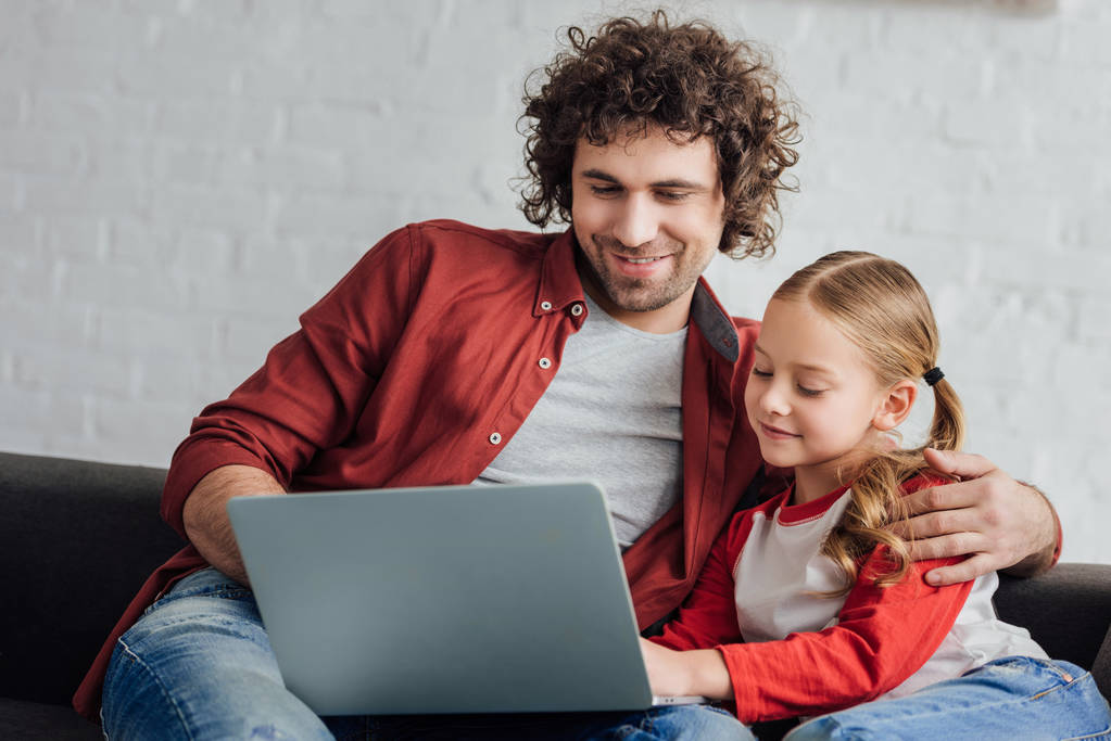 ευτυχισμένος πατέρας και η κόρη που χρησιμοποιούν φορητό υπολογιστή μαζί στο σπίτι - Φωτογραφία, εικόνα