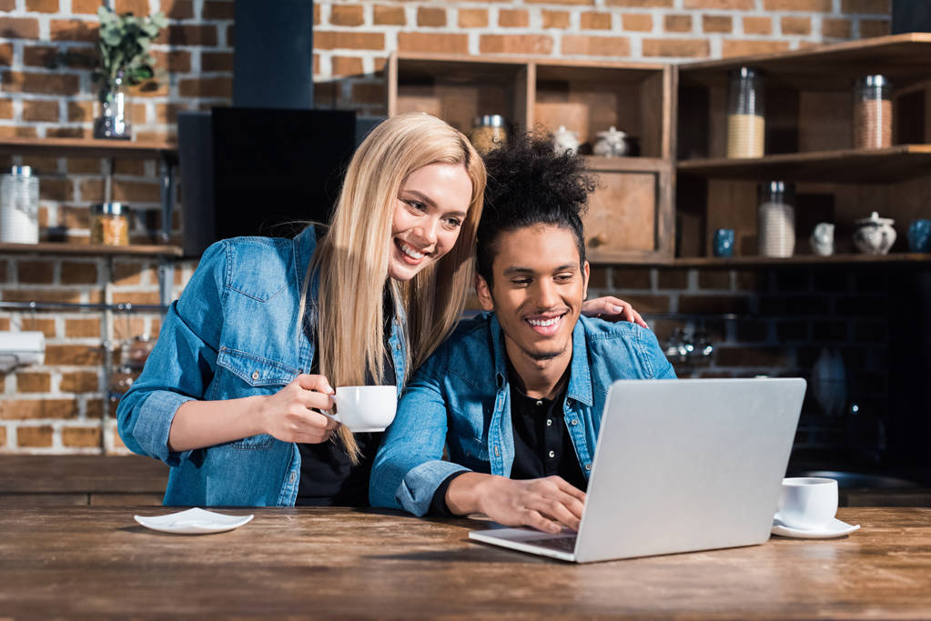 sorrindo casal multirracial usando laptop juntos na cozinha em casa
 - Foto, Imagem