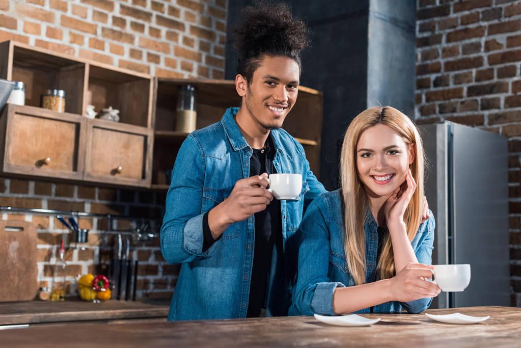ritratto di giovane coppia multirazziale sorridente con tazze di caffè in cucina a casa
 - Foto, immagini