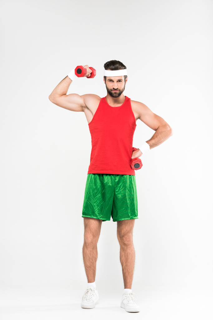 apuesto deportista en ropa deportiva retro mostrando músculos mientras entrena con pesas, aislado en blanco
 - Foto, Imagen