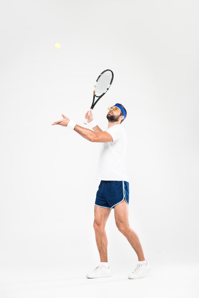 Αθλητικός άνδρας σε ρετρό γυαλιά ηλίου που παίζει τένις, απομονώνονται σε λευκό  - Φωτογραφία, εικόνα
