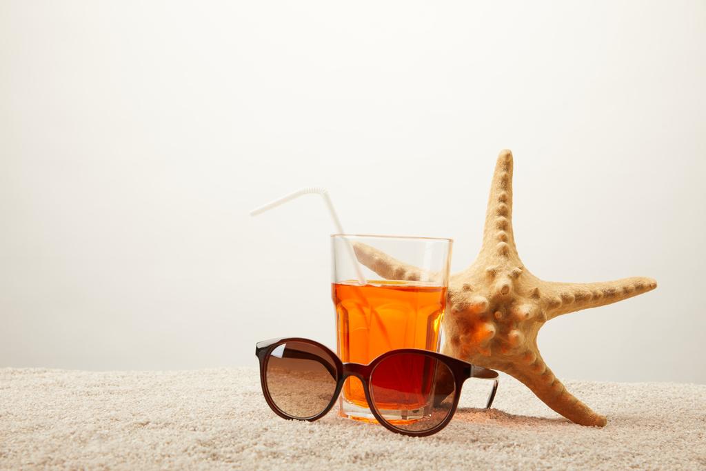 крупним планом сонячні окуляри, коктейль з соломою і морською зіркою на піску на сірому фоні
 - Фото, зображення