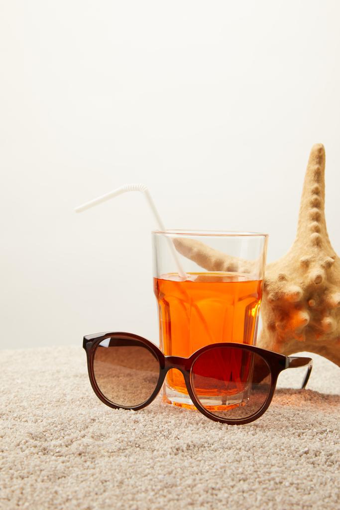 Nahaufnahme Sonnenbrille, Cocktail mit Stroh und Seestern auf Sand vor grauem Hintergrund - Foto, Bild
