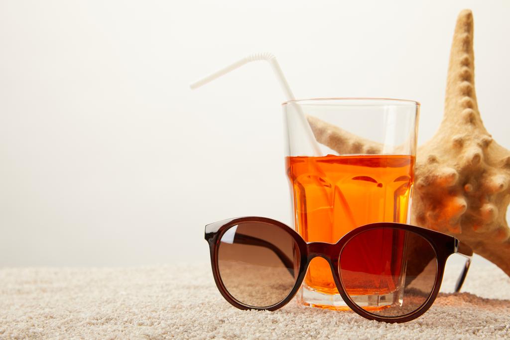 close up view of sunglasses, cocktail with straw and sea star on sand on grey backdrop - Photo, Image