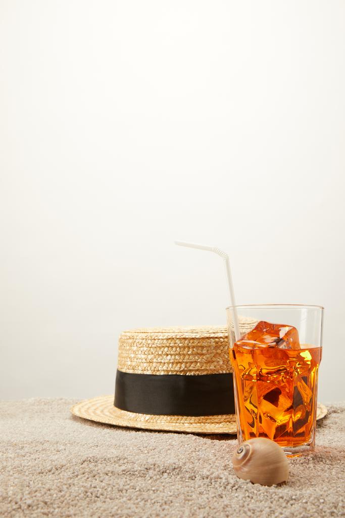 close up view of straw hat and refreshing cocktail with ice on sand on grey backdrop - Photo, Image