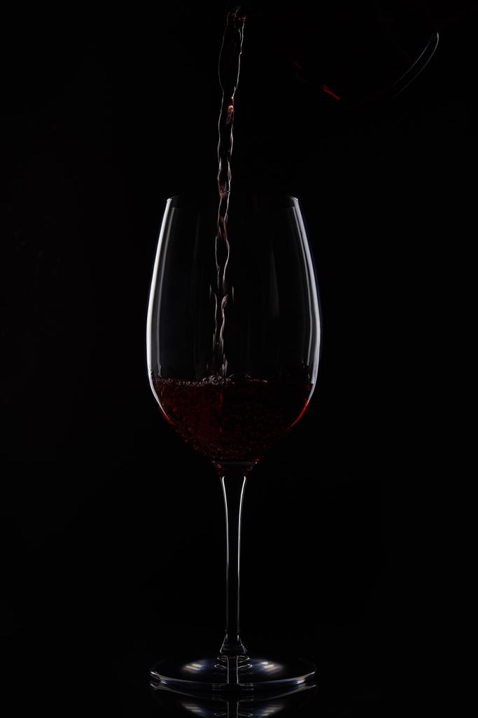 closeup βολή του κόκκινου κρασιού που ρίχνει στο γυαλί από μπουκάλι που απομονώνονται σε μαύρο φόντο - Φωτογραφία, εικόνα