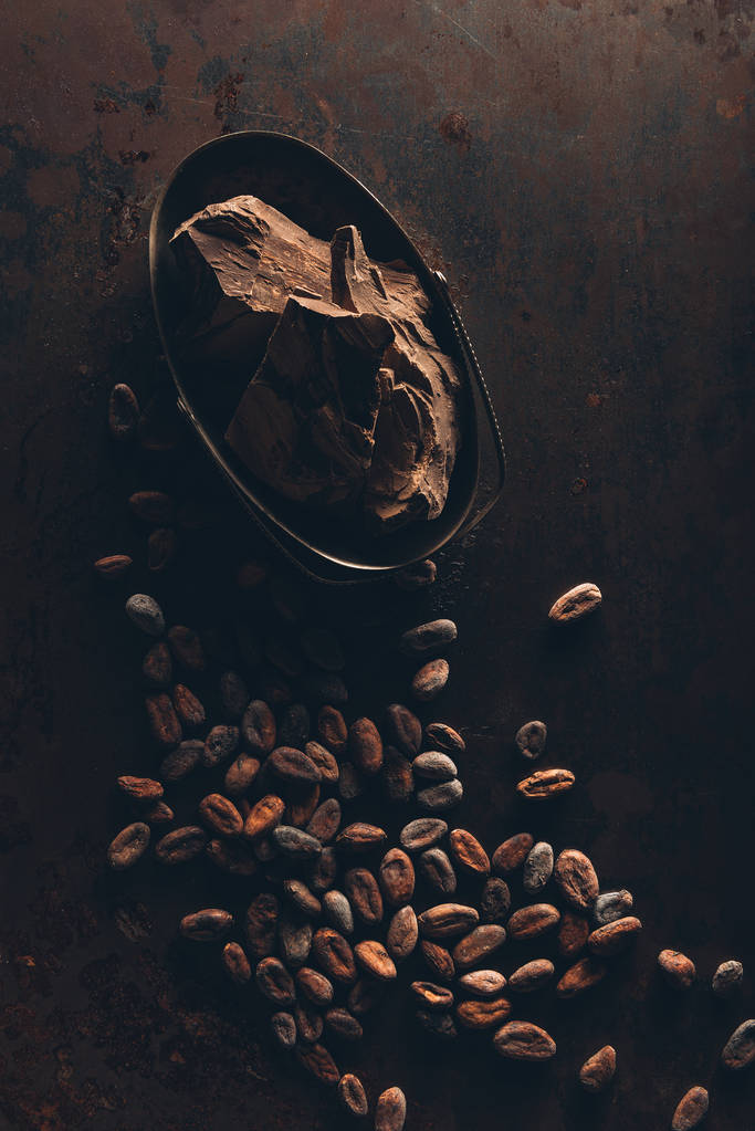 вид сверху на вкусные кусочки шоколада и какао-бобы на темной поверхности
 - Фото, изображение