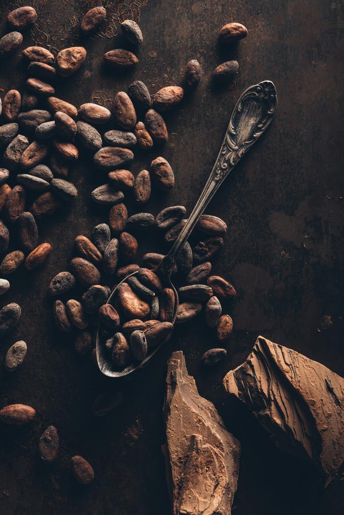 pohled shora z kakaových bobů, vintage lžíce a kousky čokolády na tmavý podklad - Fotografie, Obrázek