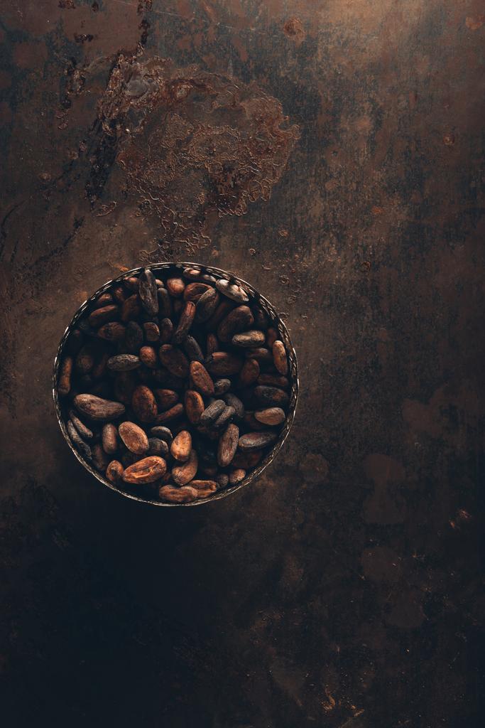 Draufsicht auf köstliche Kakaobohnen in Vintage-Schale auf dunkler rustikaler Oberfläche - Foto, Bild