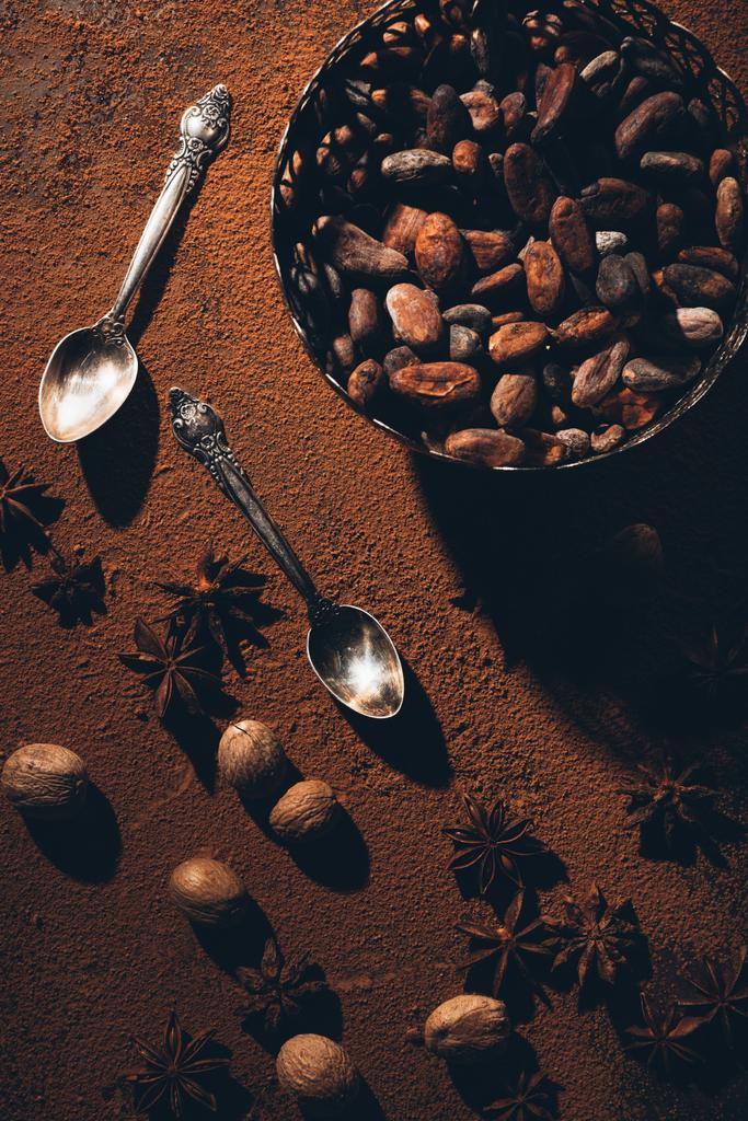 top view of cocoa beans in bowl, vintage spoons and star anise on cocoa powder - Photo, Image