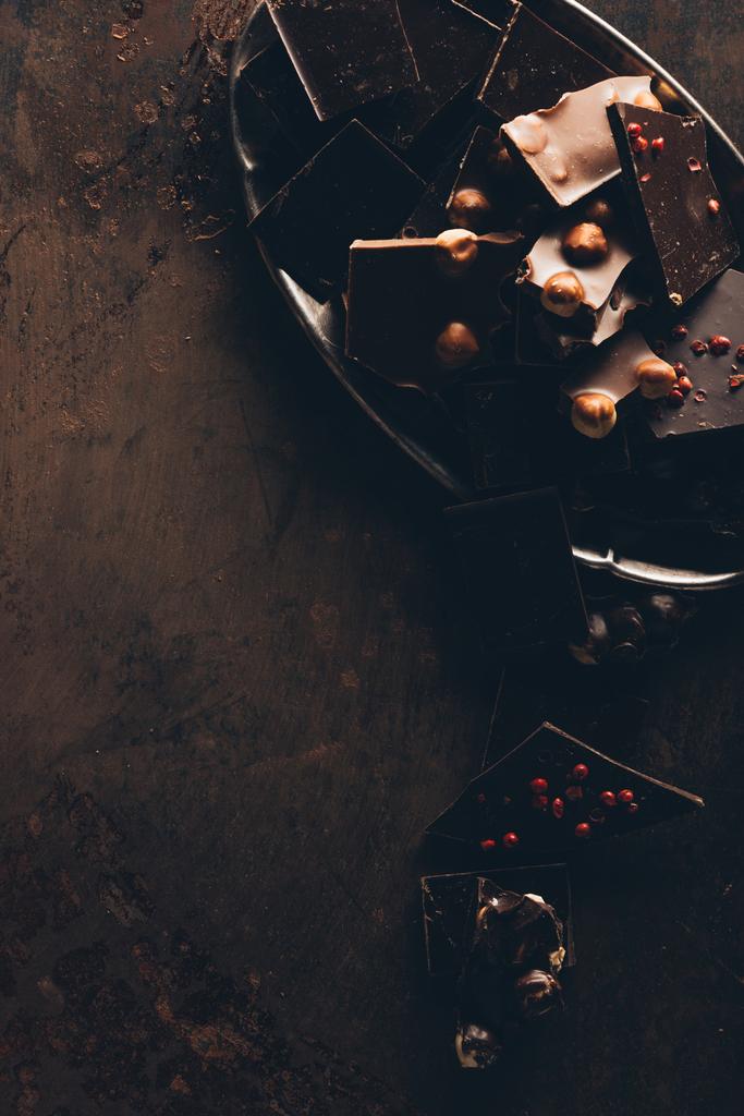 κάτοψη του τοποθετημένα διάφορα νόστιμα κομμάτια σοκολάτας με ξηρούς καρπούς στην σκοτεινή επιφάνεια - Φωτογραφία, εικόνα