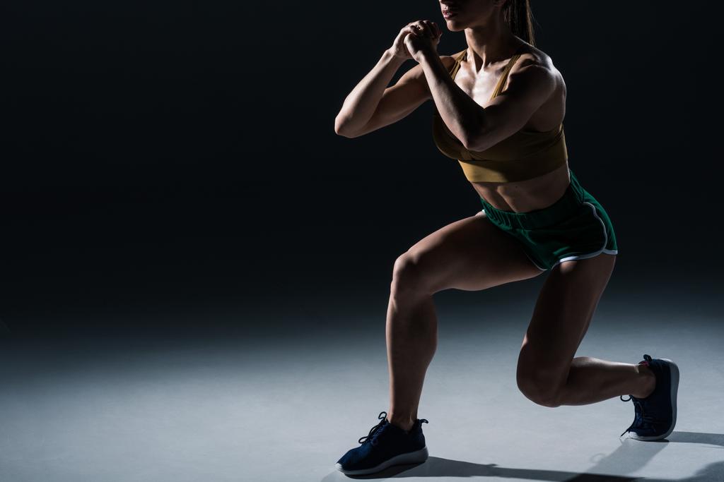 cropped view of sporty female bodybuilder doing lunges, on black    - Photo, Image