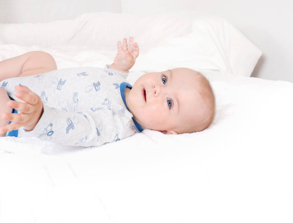Close-up portrait of sweet newborn infant lying quietly on white bed serious looking away. Happy smiling child with blue eyes on white bed background - Fotografie, Obrázek
