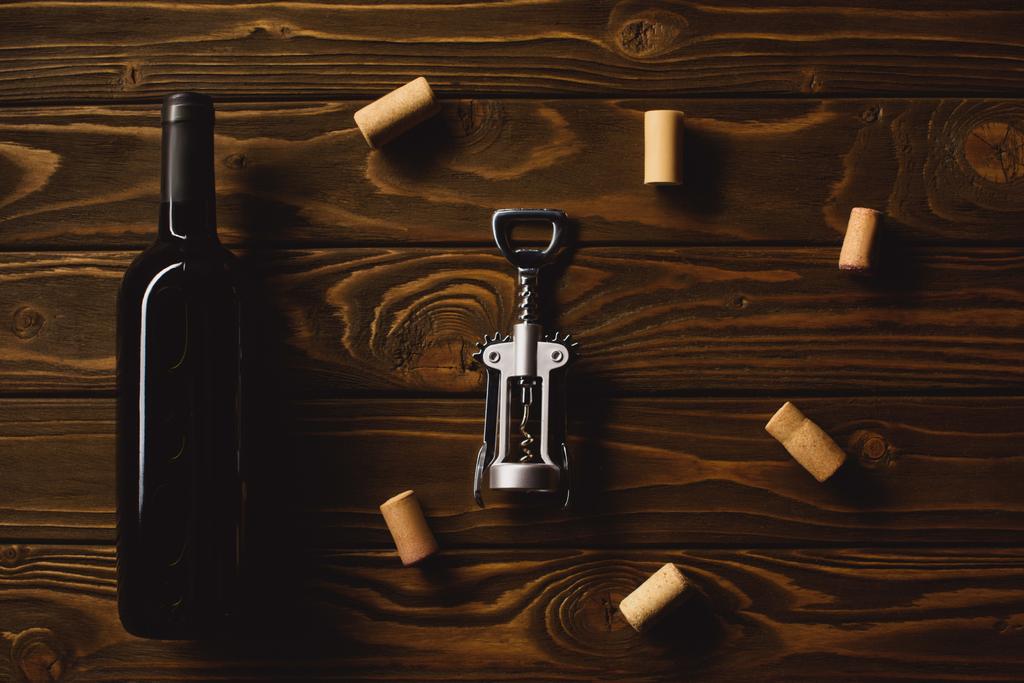 Draufsicht auf eine Flasche Luxus-Rotwein mit Korkenzieher umgeben von Korken auf einem Holztisch - Foto, Bild